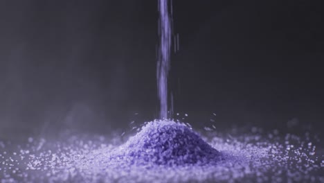 Video-of-close-up-of-purple-sand-grains-pouring-into-heap-and-copy-space-on-black-background