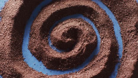 Video-of-close-up-of-brown-sand-grains-and-copy-space-in-swirl-on-blue-background