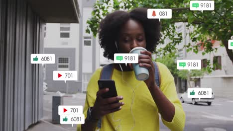 Animation-Von-Social-Media-Symbolen-Auf-Einer-Afroamerikanischen-Frau,-Die-Auf-Der-Straße-Kaffee-Mit-Ihrem-Smartphone-Trinkt