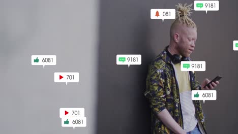 Animation-Von-Social-Media-Symbolen-über-Einem-Albino-Mann-Mit-Smartphone,-Der-Vor-Einer-Grauen-Wand-Steht