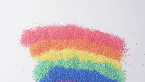 Video-of-close-up-of-rainbow-coloured-sand-grains-and-copy-space-on-white-background