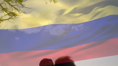 Animation-of-waving-colombia-flag-against-biracial-couple-kissing-at-the-beach