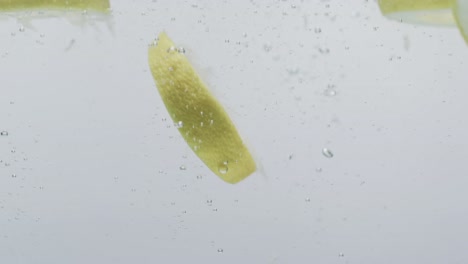Video-of-slices-of-lime-and-lemon-falling-into-water-with-copy-space-on-white-background
