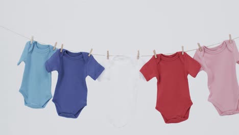 Video-of-multi-coloured-baby-grows-hanging-on-pegs-from-line-with-copy-space-on-white-background