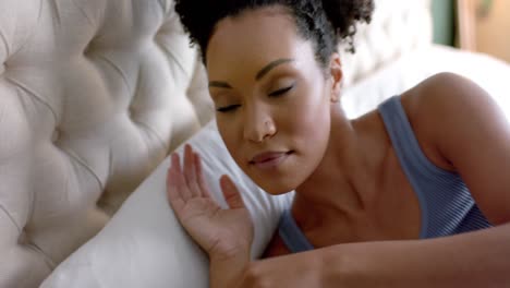 Biracial-woman-taking-nap-in-bed-in-bedroom,-slow-motion