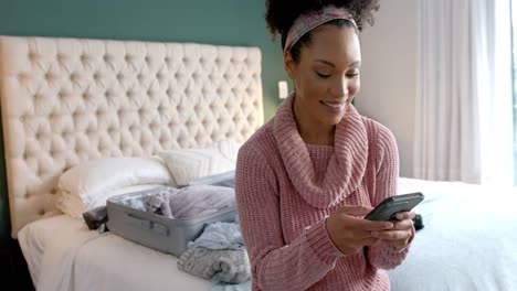 Happy-biracial-woman-using-smartphone-in-sunny-bedroom,-slow-motion