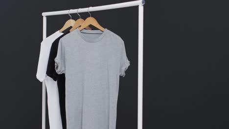 Video-of-three-white,-black-and-grey-t-shirts-on-hangers-and-copy-space-on-black-background