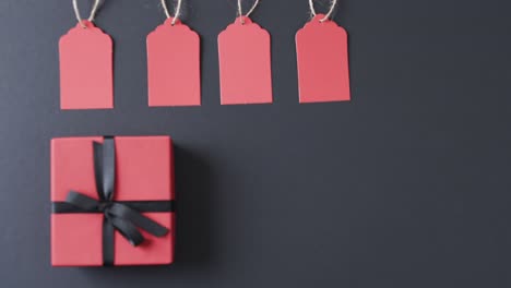 Video-of-gift-tags-on-string,-red-gift-box-with-ribbon-and-copy-space-on-black-background