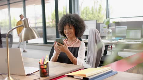 Mujer-Afroamericana-Usando-Un-Teléfono-Inteligente-Sentada-En-Su-Escritorio-En-La-Oficina