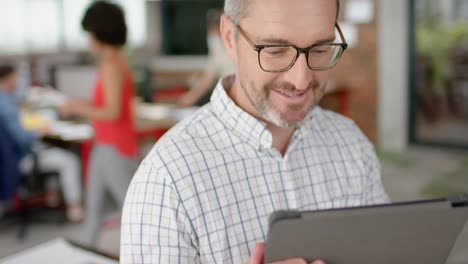 Portrait-of-caucasian-man-using-a-digital-tablet-and-smiling-at-office