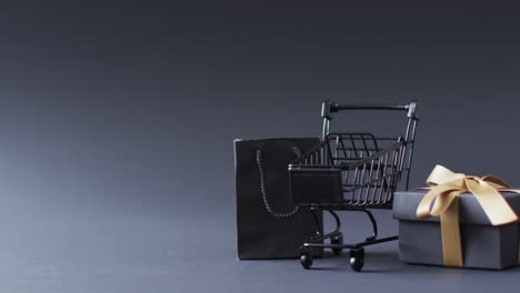 Video-of-shopping-trolley,-shopping-bag-and-gift-box-with-copy-space-over-grey-background