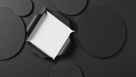 Vertical-video-of-circles-of-black-paper-and-square-cut-out-with-copy-space-on-white-background