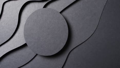 Video-of-close-up-of-circle-of-black-paper-on-waves-cut-out-and-copy-space-on-black-background