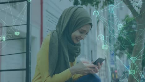 Animation-of-changing-numbers,-connected-icons-globe,-biracial-woman-wearing-hijab-using-cellphone