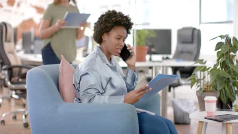 African-american-casual-businesswoman-with-documents-talking-on-smartphone-in-office,-slow-motion
