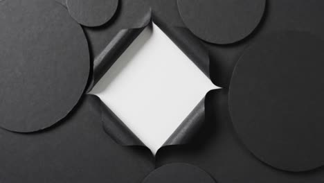 Vertical-video-of-circles-of-black-paper-and-square-cut-out-with-copy-space-on-white-background