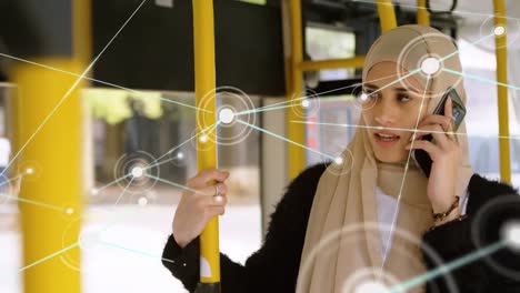 Animation-of-connected-dots,-biracial-woman-wearing-hijab-talking-on-phone-while-travelling-on-bus