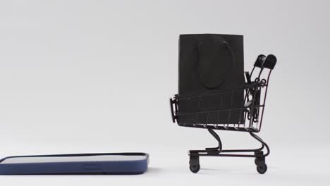 Video-Von-Smartphone,-Einkaufstasche-Und-Trolley-Mit-Kopierraum-Auf-Weißem-Hintergrund