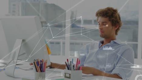 Animation-of-connected-dots-and-graph-icons-over-caucasian-man-working-on-desktop-in-office