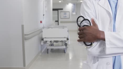 Midsection-of-african-american-male-doctor-in-hospital-corridor-with-copy-space,-slow-motion