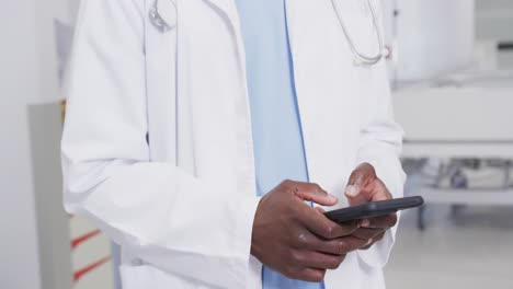 Mittelteil-Eines-Afroamerikanischen-Männlichen-Arztes,-Der-Im-Krankenhaus-Sein-Smartphone-Benutzt,-Zeitlupe
