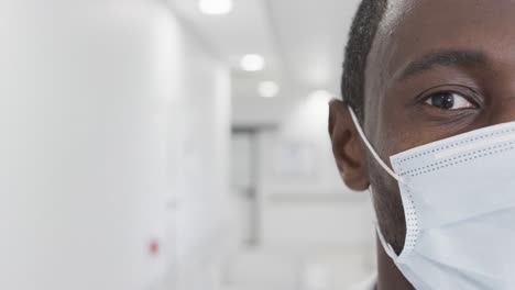 Half-portrait-of-african-american-male-doctor-with-face-mask-in-hospital,-copy-space,-slow-motion