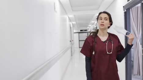 Caucasian-female-doctor-taking-off-face-mask-walking-in-hospital-corridor,-slow-motion