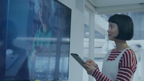 Animation-of-bar-graph-over-asian-woman-looking-at-television-and-using-digital-tablet-in-office