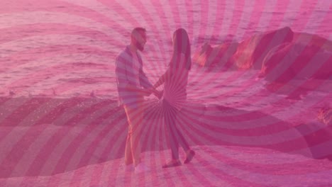 Animation-of-pink-sunbeam-pattern-over-diverse-couple-holding-hand-and-standing-near-sea