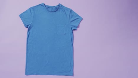 Video-Eines-Blauen-T-Shirts-Mit-Etikett-Und-Kopierraum-Auf-Violettem-Hintergrund