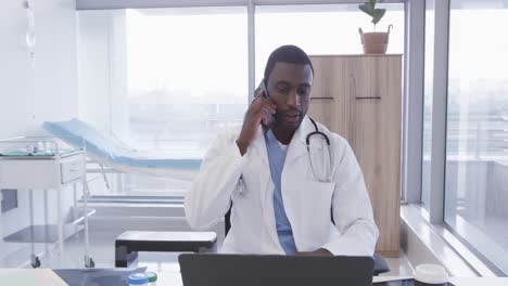 Afroamerikanischer-Männlicher-Arzt,-Der-Im-Krankenhausbüro-Auf-Dem-Smartphone-Spricht,-Zeitlupe
