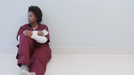 Tired-african-american-female-doctor-with-face-mask-sitting-in-hospital-corridor,-slow-motion