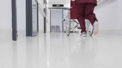 African-american-female-doctor-running-with-wheelchair-in-hospital-corridor,-slow-motion