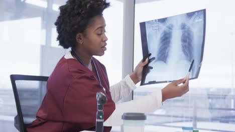 African-american-female-doctor-holding-x-ray-image-making-video-call-in-hospital-office,-slow-motion