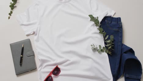Video-Von-Weißem-T-Shirt,-Jeanshose,-Notizbuch,-Sonnenbrille-Und-Kopierraum-Auf-Weißem-Hintergrund