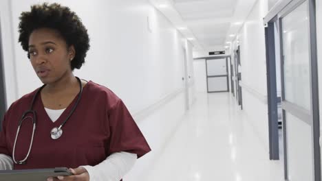 Doctora-Afroamericana-Usando-Tableta-Caminando-En-El-Pasillo-Del-Hospital,-Cámara-Lenta