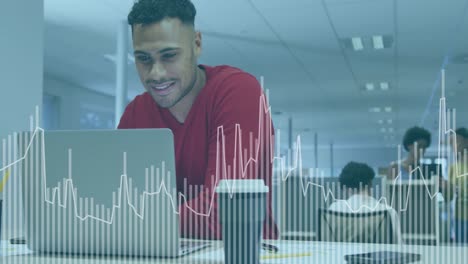 Animation-of-graphs-over-smiling-biracial-man-standing-and-using-laptop-in-office