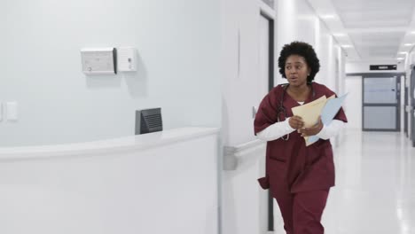 African-american-female-doctor-holding-documents-running-in-hospital-corridor,-slow-motion