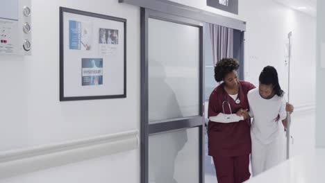Afroamerikanische-Ärztin-Hilft-Patientin-Beim-Gehen-Im-Krankenhauskorridor,-Zeitlupe
