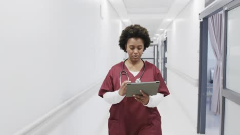 African-american-female-doctor-using-tablet-walking-in-hospital-corridor,-slow-motion