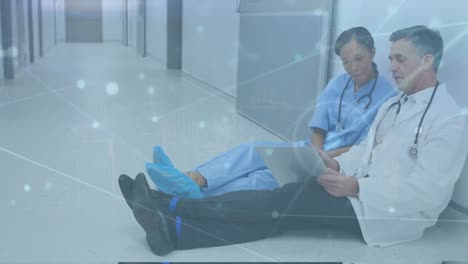 Animation-of-connected-dots-over-diverse-doctors-discussing-report-on-laptop-and-sitting-on-floor