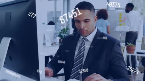 Animation-of-multiple-changing-numbers-over-biracial-man-working-on-desktop-in-office