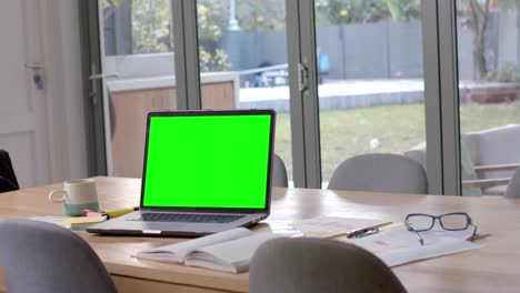 Laptop-with-green-screen,-glasses-and-paperwork-on-dining-table,-slow-motion