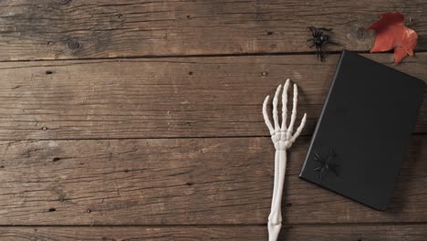 Video-of-halloween-skeleton-hands,-notebook-and-decorations-with-copy-space-on-wooden-background