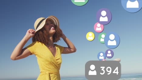 Animation-of-changing-numbers,-profile-icons,-happy-biracial-woman-standing-at-beach-against-sky