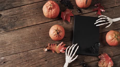 Video-of-halloween-skeleton-hands,-notebook-and-decorations-with-copy-space-on-wooden-background