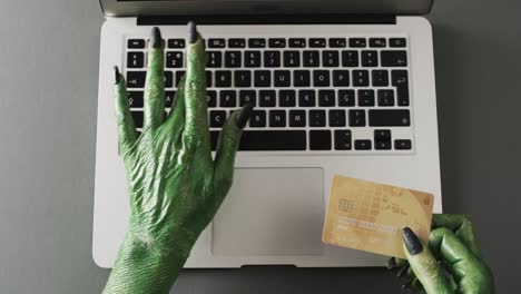 Video-of-halloween-green-monster-hands-holding-card-and-laptop-with-copy-space-on-grey-background