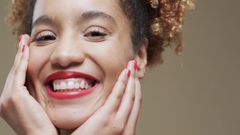 Happy-biracial-woman-with-dark-hair-and-red-lips-and-nails-on-beige-background,-slow-motion