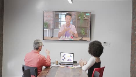 Diverse-business-people-on-video-call-with-caucasian-male-colleague-on-tv-screen