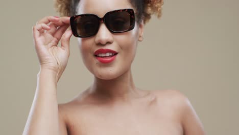 Biracial-woman-with-dark-curly-hair-and-sunglasses-with-copy-space-on-beige-background,-slow-motion